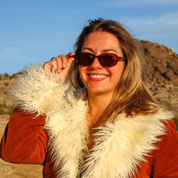 Woman wearing sunglasses and a red coat with a fur collar in a desert setting