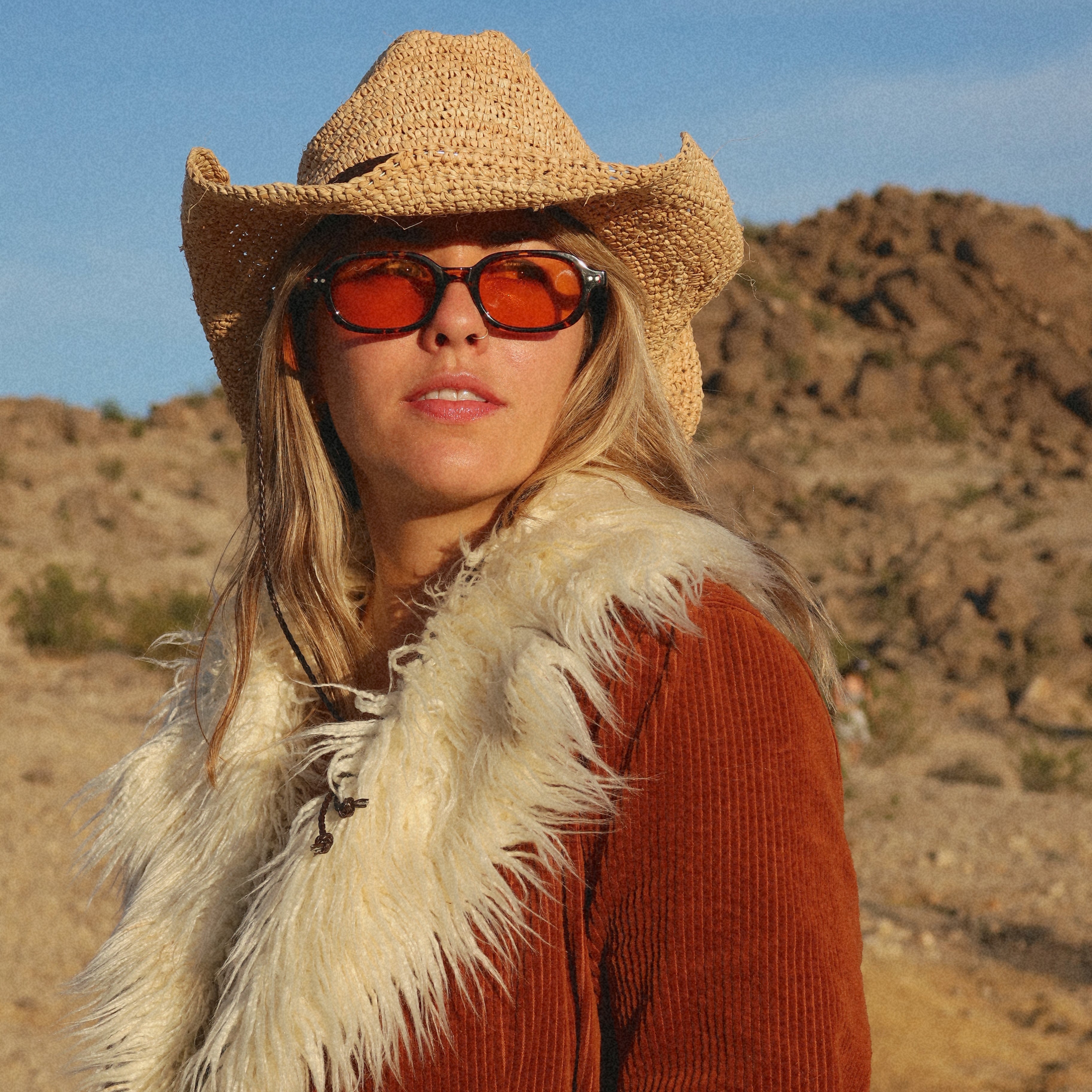 Person wearing a cowboy hat and sunglasses in a desert setting