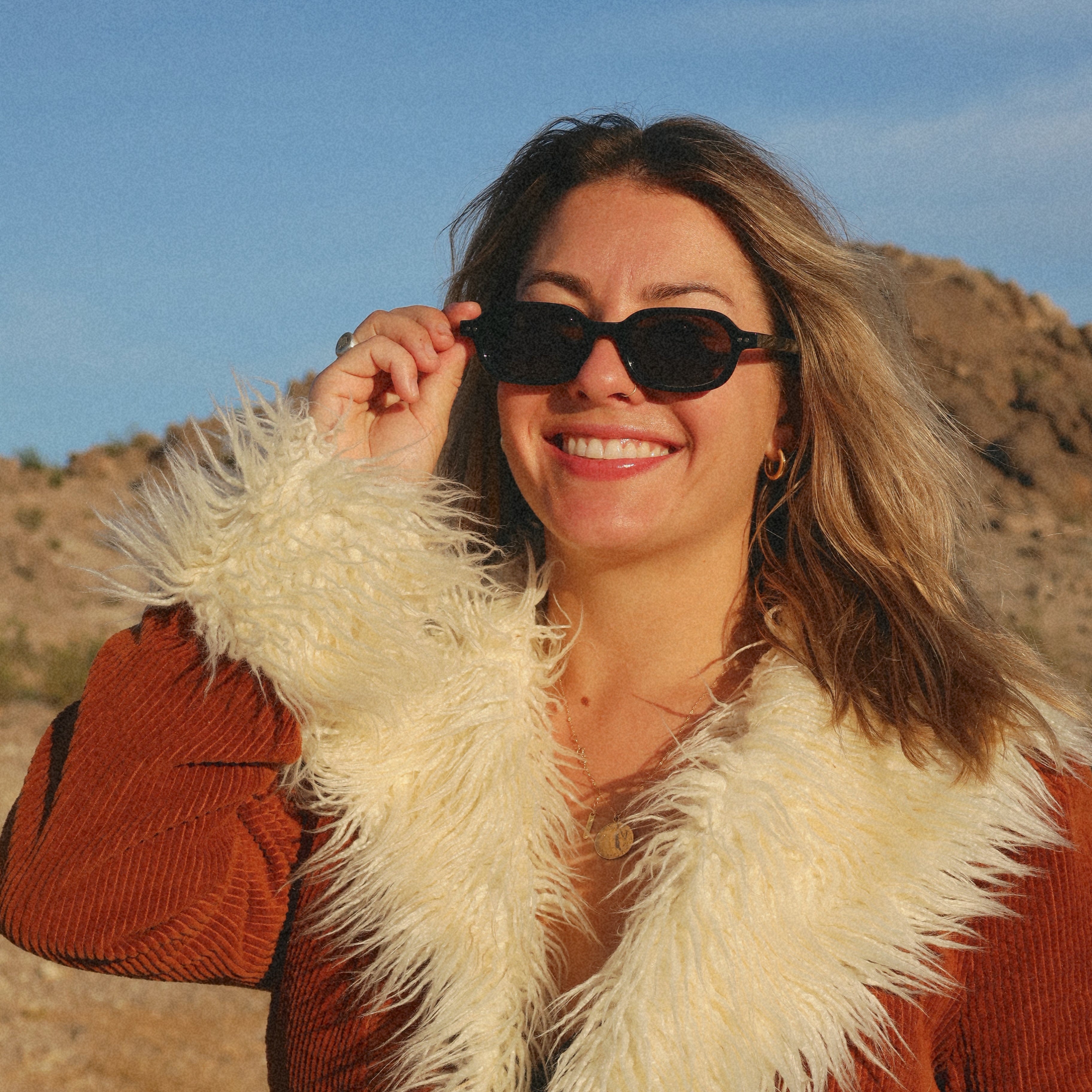 Woman wearing sunglasses and a fur scarf in a desert setting
