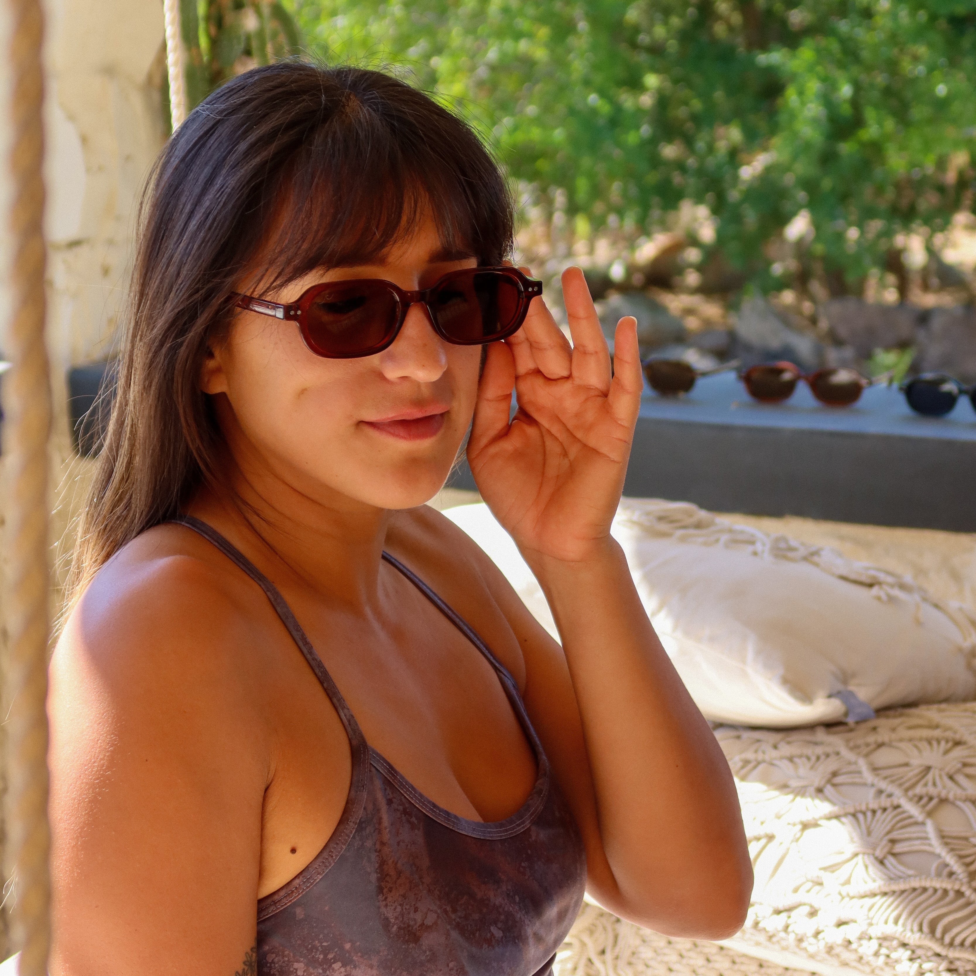 Woman wearing sunglasses outdoors with greenery in the background