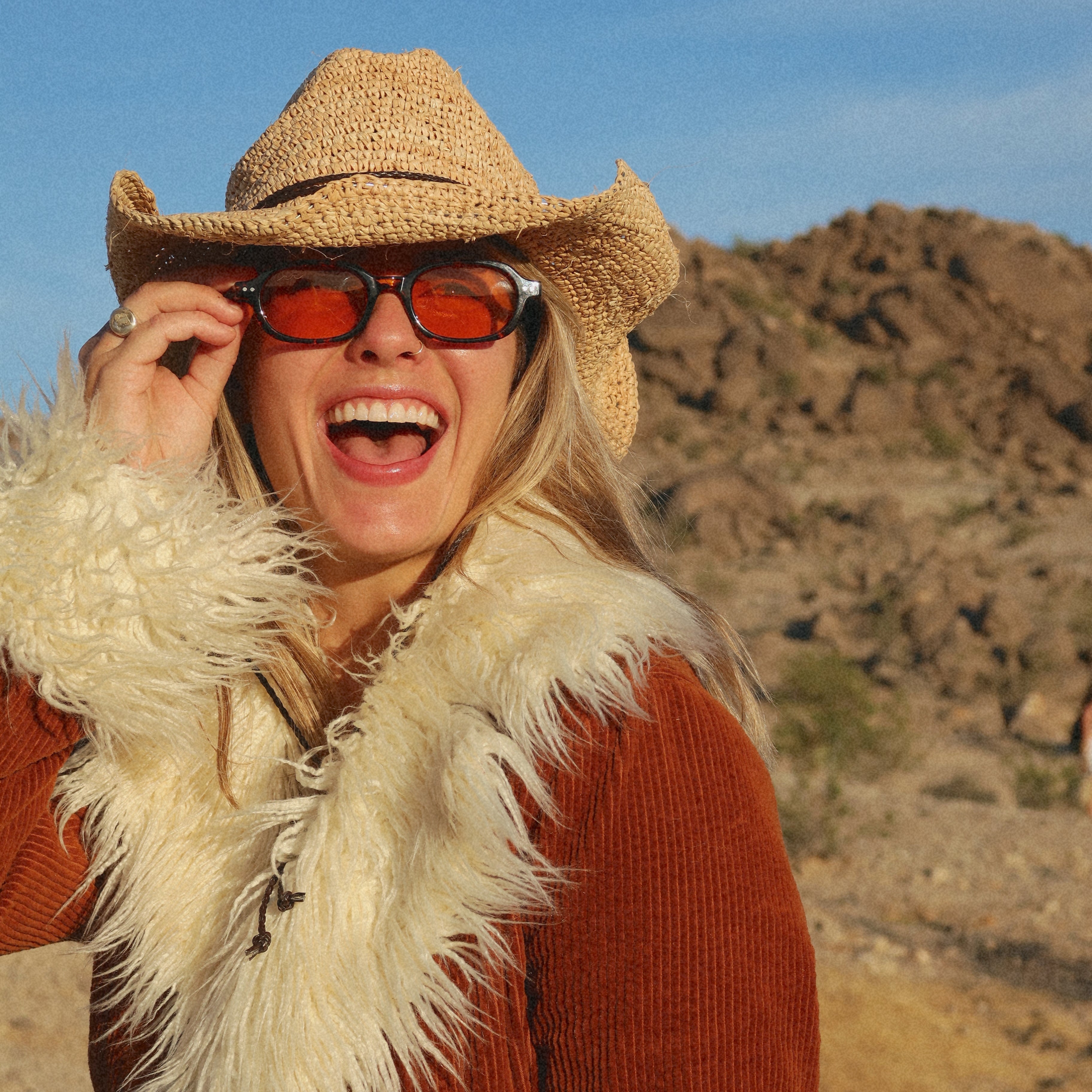 Person wearing a cowboy hat and sunglasses with a desert landscape in the background