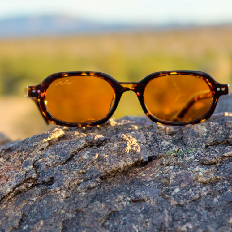 Sunglasses with amber lenses on a rock with a blurred natural background